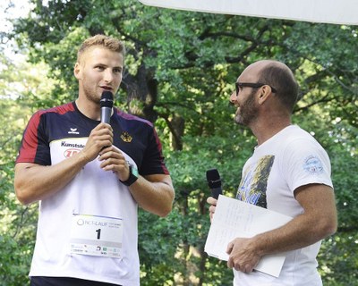 (c) UKDD (Ulrich Lippke) Zwei Männer im Freien, einer mit Mikrofon und Laufnummer auf Sportshirt, der andere mit Mikrofon und Notizblock, im Gespräch