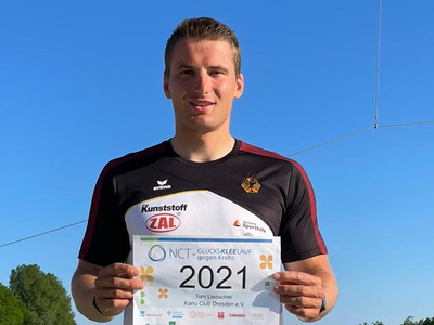 Tom Liebscher (c) agentursenderundempfänger Junger Mann in Sportshirt mit deutscher Adler-Emblem hält Startnummer 2021 vor blauem Himmel und grüner Landschaft