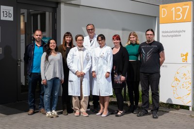 Group of nine people including three in white lab coats standing in front of a building